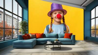 Funny child clown, hat and a red nose. Cheerful little girl on a yellow background. April 1. April Fools Day. Copy space Wall mural