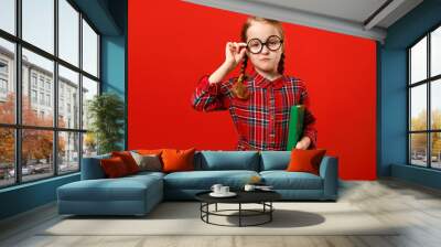 Funny child in glasses and with a book on a red background. Portrait of a serious smart little girl Wall mural