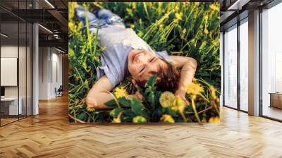 preschooler boy lies in grass in blooming dandelions and smilesv Wall mural