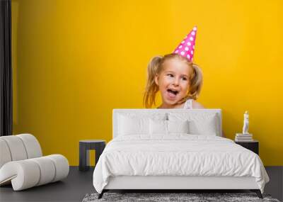 Happy birthday child girl with two ponytales in pink cap on colored yellow background shoing her tongue. Wall mural