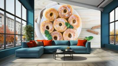 Homemade ring-shaped sugared donuts on a white plate on a light wooden background, rustic style Wall mural