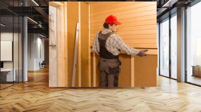 Sauna construction, finishing. The man is screwing a wooden bench to the wall. Wall mural