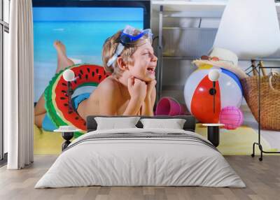 boy with inflatable beach toys imitatiing of oversea vacation beach in front of tv that shows image  Wall mural