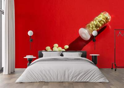 A bottle of yellow pills. Tablets are scattered on a red background. Wall mural