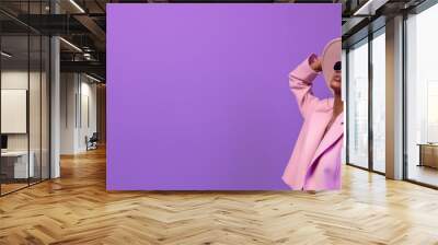 Woman wearing pink clothes and hat in dark sunglasses looking up on pastel purple background, fashion photography. Wide banner with copy space for web design or beauty magazine article. Wall mural