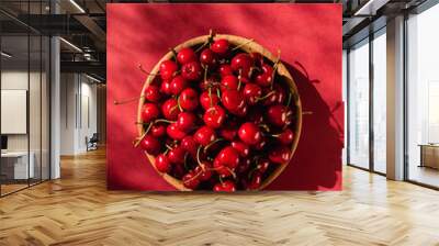 Top view on ripe sweet cherries in wooden bowl in sunlight on red background. Wall mural