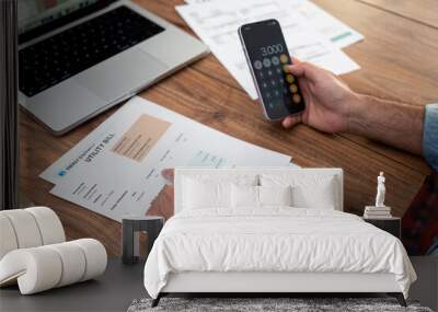 Close-up of a man calculating household utility bills using a smartphone. Financial management and budgeting concept for household expenses and utility bills Wall mural