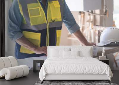 Engineer in vest studying project documentation getting ready for apartment reconstruction man reading papers near protective hardhat construction safety equipment Wall mural