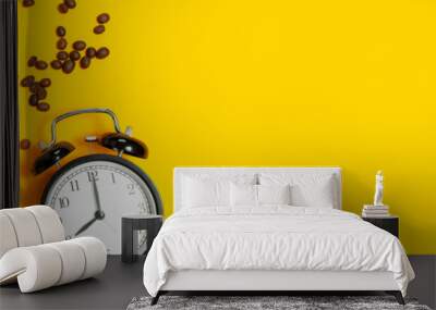 Flat lay cup of black coffee, coffee beans, black alarm clock on yellow background top view copy space. Minimalistic food concept, morning breakfast, time to work, hot drink, coffee background Wall mural