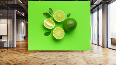 Fresh juicy lime and green leaves on bright green background. Top view flat lay copy space. Creative food background, tropical fruit, vitamin C, citrus. Composition with whole and slices of lime Wall mural