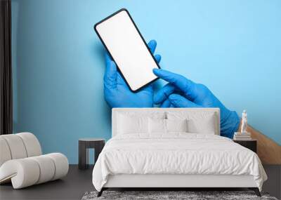 Male hands in blue medical gloves hold smartphone with white blank screen on blue background. Safety protection against bacteria during the virus, coronavirus 2019-nCoV. Hands doctor with phone Wall mural