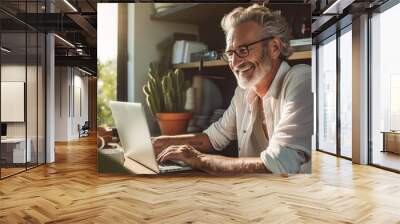 A happy pensioner man sits in his home office at a computer, works as a freelancer, or communicates via video on the Internet. Life style of elderly people concept. Wall mural