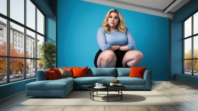 Beautiful blonde woman plus size model posing on blue background Wall mural