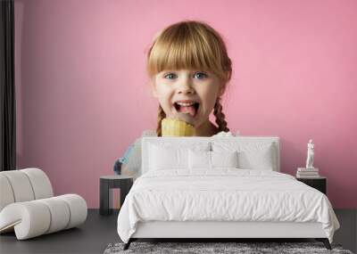 little girl with pigtails in a blue dress eating ice cream in a cone on a pink background Wall mural