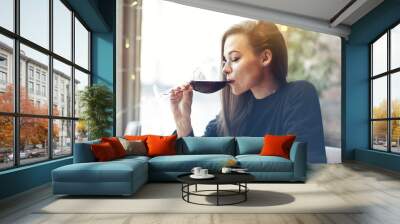 Beautiful young woman drinking red wine with friends in cafe, portrait with wine glass near window. Vocation holidays evening concept Wall mural