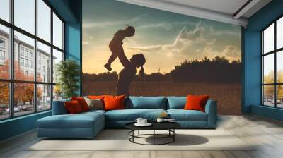 Silhouette of a young mother and her little daughter at sunset Wall mural