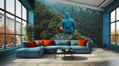 A man in a blue jacket sits on top of a mountain and admires the view Wall mural