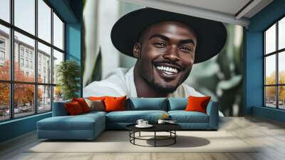 A man with a black hat and a white shirt is smiling in front of a plant Wall mural