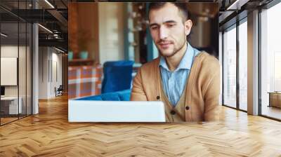 A young man works behind a laptop in a cozy cafe. Business and coworking concept. Portrait of a man. Wall mural