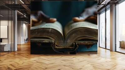 of close-up of a black anonymous person hands gently turning the pages of an open book on table with a warm light overhead Wall mural