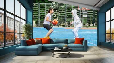 Girl and her younger brother, teenager, play basketball on modern basketball court under open sky Wall mural