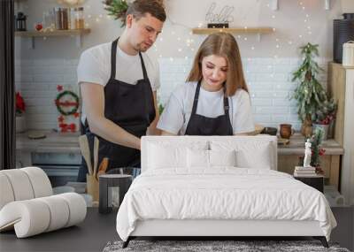 Young happy couple enjoying and preparing christmas cookies together in their kitchen. Wall mural