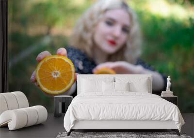 portrait of a charming blonde teenage girl with a fresh orange outdoors in forest or park. tasty juicy fruit Wall mural