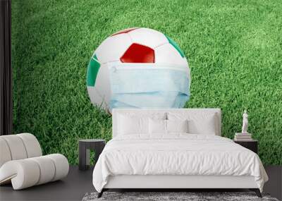 Soccer ball in italian colors with mask on green field. Virus threatened championship concept Wall mural