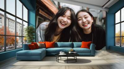 two young asian girls laughing out loud teenagers friends outdoors smiling happy city street lipstick casual jackets bright light complicity bond friendship enjoying cheerful upbeat youth joy joyful Wall mural