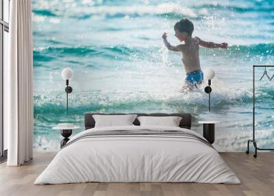 A little boy on the beach, playing with the waves Wall mural