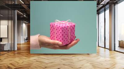 woman's hand giving pink gift box in polka dots Wall mural