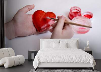 The child paints a decorative heart with red paint. Preparing for Valentine's Day. Wall mural