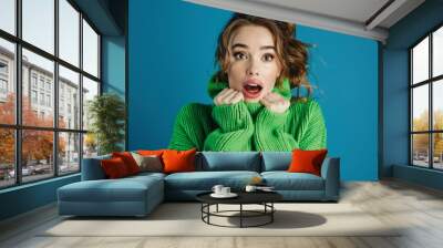 Surprised young woman in cozy green sweater against blue background. Excited expression and casual style. Perfect for lifestyle concepts and fashion themes. Generative AI Wall mural