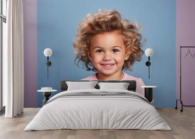 Cute smiling little child with blond curly hair in pink t-shirt on blue background with copy space Wall mural