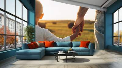 Father's and his son holding hands at sunset field. Dad leading son over summer nature outdoor. Family, trust, protecting, care, parenting concept Wall mural