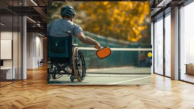 Male wheelchair athlete with racket on Pickleball court, autumnal trees in the background Wall mural