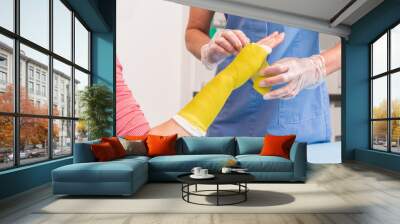 Surgery and Medical theme: Close up of an arm and wrist plaster  fiberglass cast therapy cover by yellow elastic bandage after sport accident. The nurse puts a red plaster cast on the woman arm. Wall mural