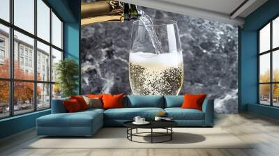 Photo of a bottle being poured into an elegant champagne glass, with the sparkling bubbles visible against grey stone tiles in a minimalist setting Wall mural