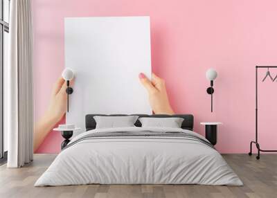 Female hands holding blank white paper sheet on pink background. Mock up Wall mural