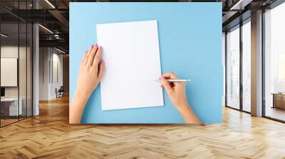 Overhead shot of female hands writing with pen over empty white sheet of paper on blue background Wall mural