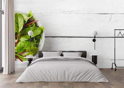 Overhead shot of fresh green salad with spinach, arugula and beetroot leaves in bowl on white wooden background with copyspace. Banner Wall mural