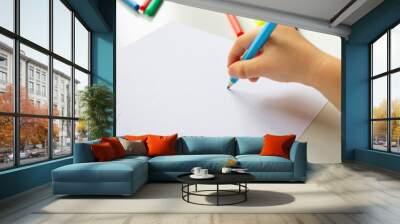 Close up of child's hands drawing at blank white paper with a blue pencil, school background Wall mural