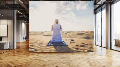 Arab man wearing typical middle eastern clothing in the desert praying for ramadan celebration Wall mural