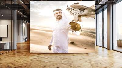 Arabic man with traditional emirates clothes walking in the desert with his falcon bird Wall mural