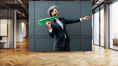 Cinematic and storytelling image of a young entrepreneur throwing a green paper aircraft in the air. Conceptual representation of green energy and technology ideas Wall mural