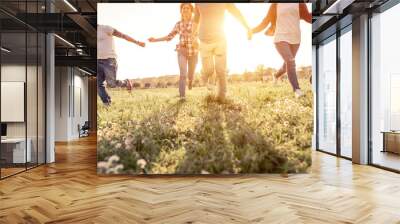 Group of friends running happily together in the grass Wall mural