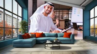 Handsome arab businessman wearing emirates kandora working at his desk in the office, Dubai Wall mural