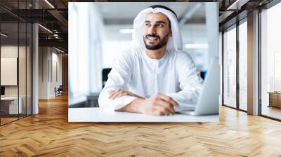 Handsome man with dish dasha working in his business office of Dubai. Portraits of a successful businessman in traditional emirates white dress. Concept about middle eastern cultures. Wall mural