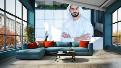 Handsome man with dish dasha working in his business office of Dubai. Portraits of a successful businessman in traditional emirates white dress. Concept about middle eastern cultures Wall mural