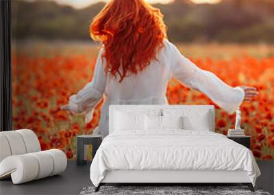 Happy redhead smiling woman in white dress on field of poppies at summer sunset Wall mural